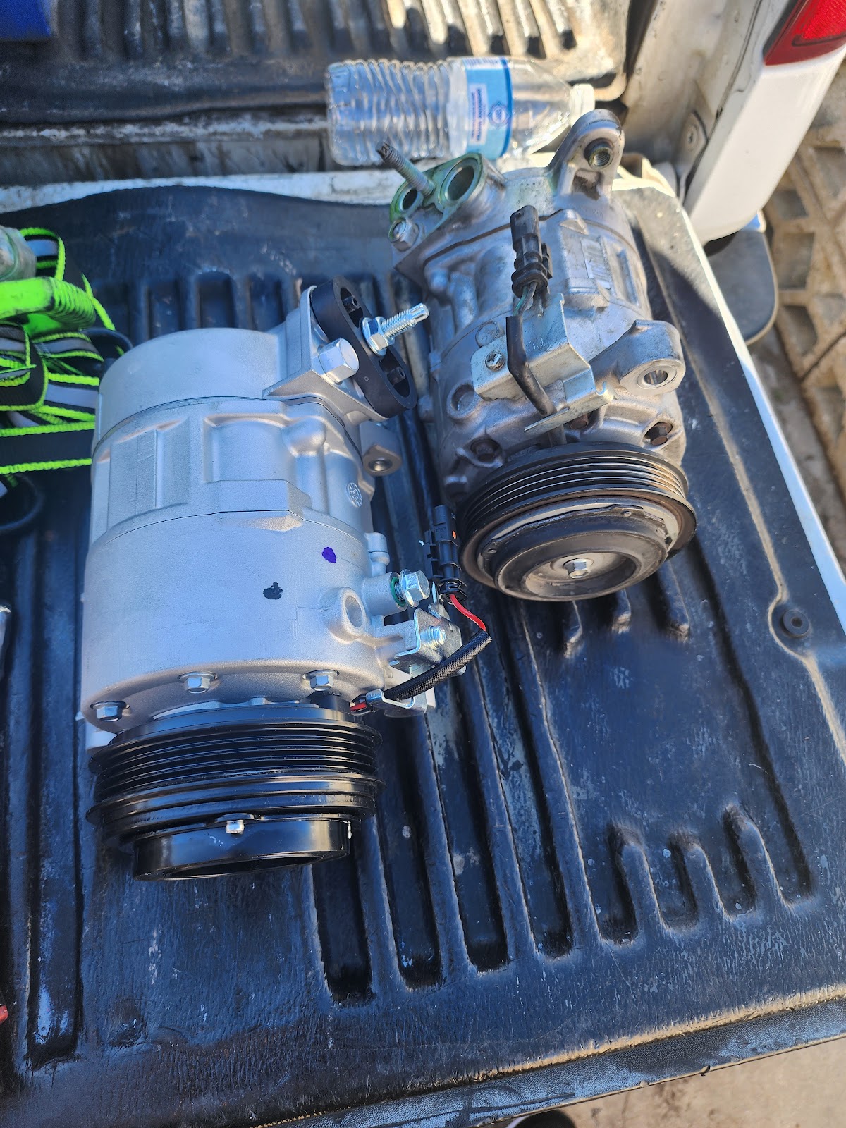 New A/C compressor next to the worn one it replaced, laid out on a truck bed
