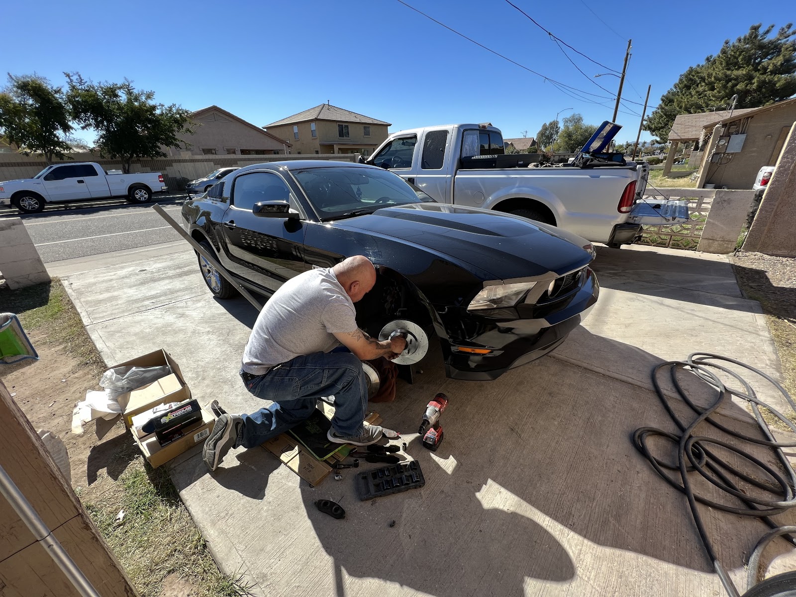 Front brake job on a black Mustang in a Peoria driveway, rotor exposed, parts boxes and tools on the concrete under full sun