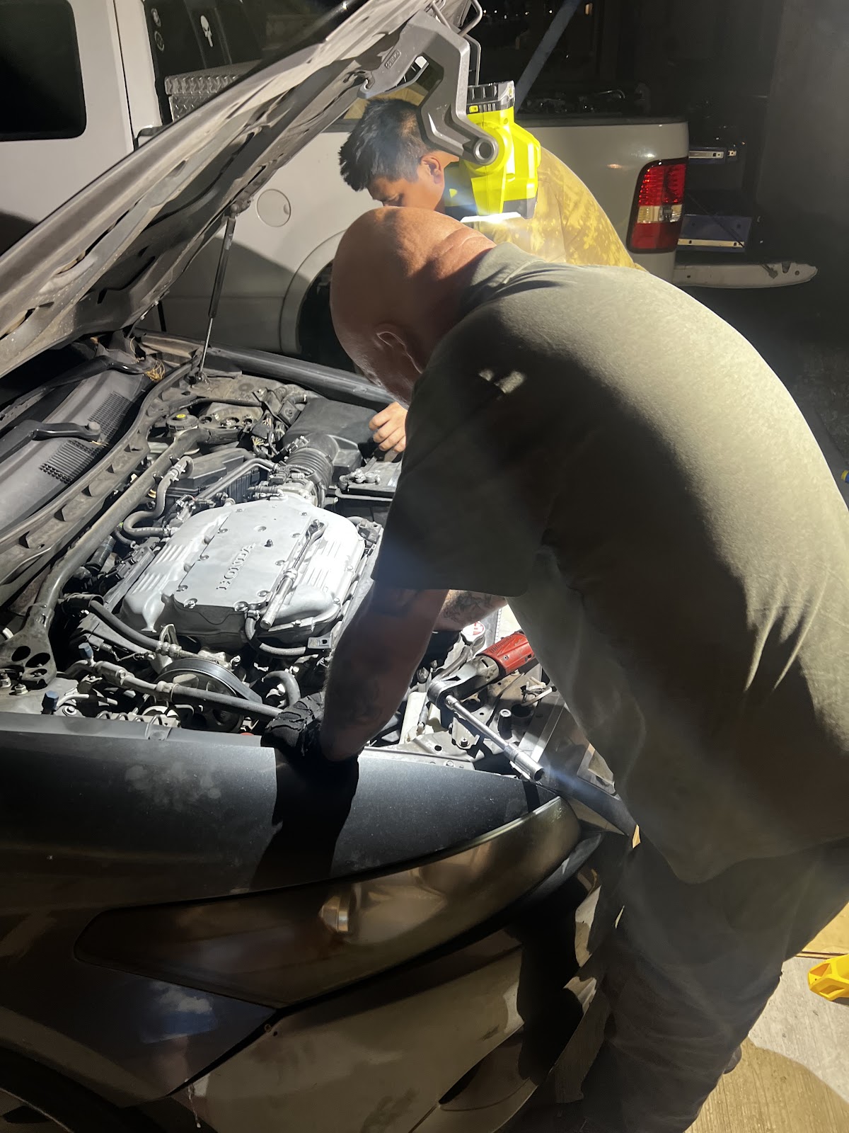 Two of us leaning into an engine bay by flashlight at night, checking a car over
